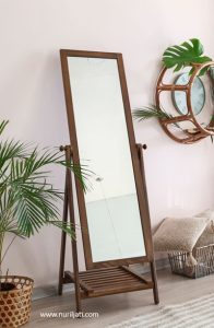 Cermin persegi panjang kayu organik besar bersandar di dinding putih di kamar tidur.