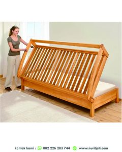 Foto kursi tamu sudut lipat modern berwarna abu-abu terang, menunjukkan mekanisme lipatnya saat diubah dari sofa sudut menjadi tempat tidur, di ruang tamu kecil.