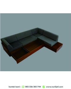 Foto kursi tamu sudut simple L-Shape berwarna abu-abu muda, berlengan rendah, diletakkan di ruang tamu minimalis dengan karpet area netral.